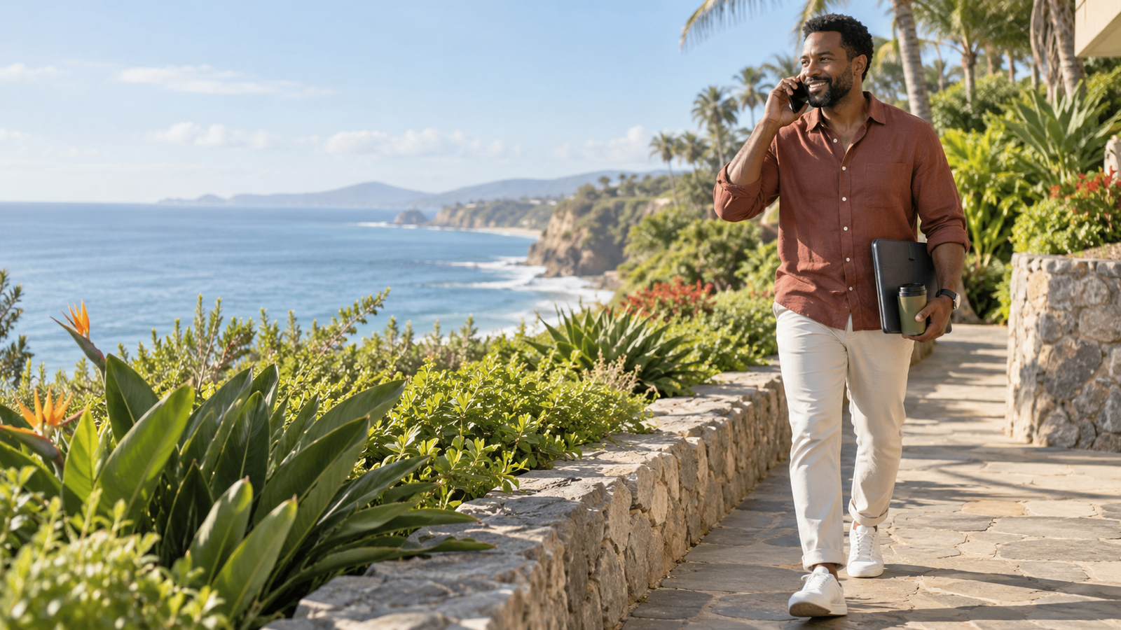 Male remote professional walking along a scenic coastal path while handling a business call.